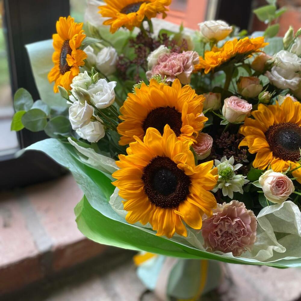 Букет из подсолнухов, эустомы, кустовой пионовидной розы, орнитогалума, седума и гвоздик в стильной упаковке 